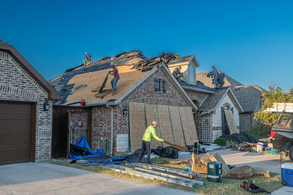Workers engage in roof replacement on a brick house